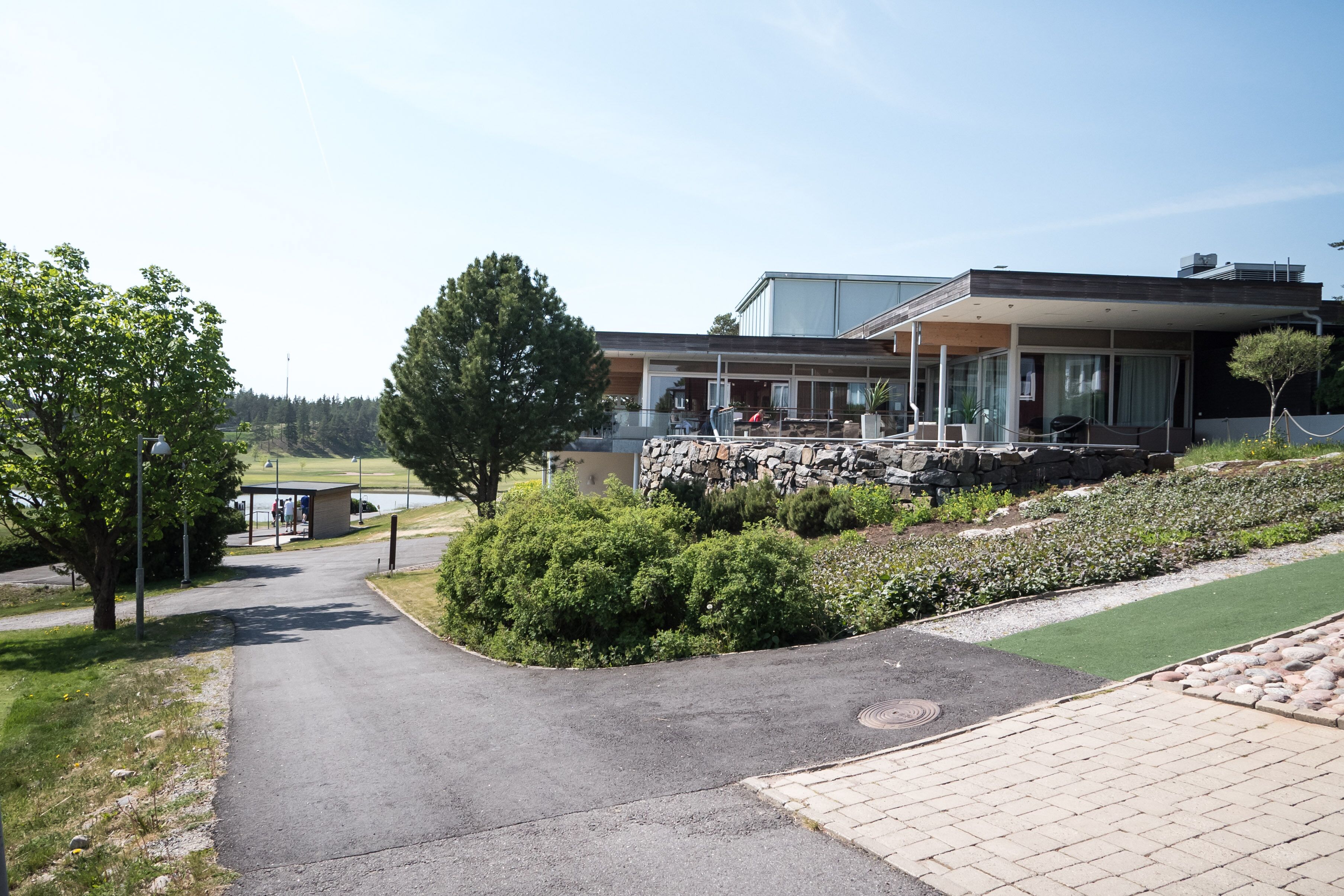 A modern building with a stone facade, a paved driveway, and a landscaped garden area.