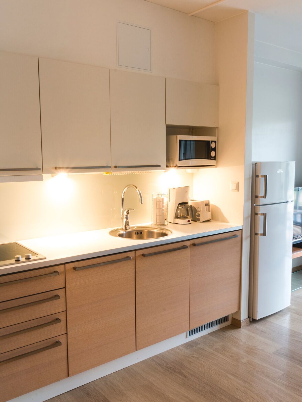 A modern kitchen with white cabinets, a stainless steel sink, a microwave, a coffee maker, and a refrigerator.