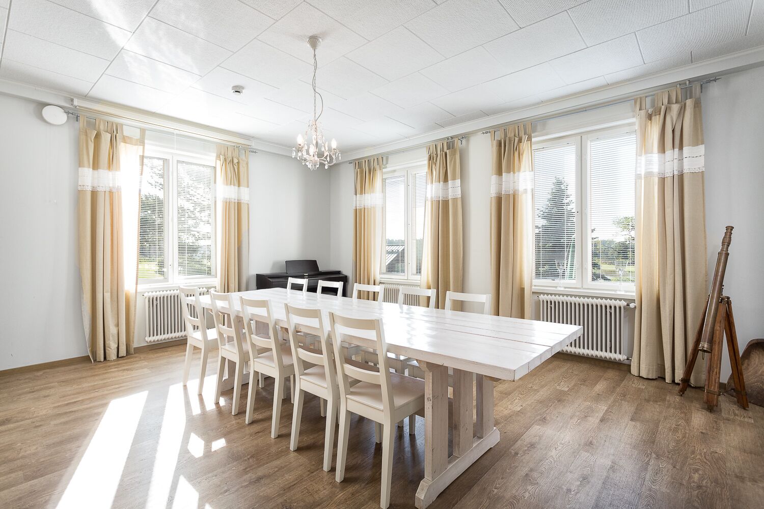 Una habitación amplia con un gran comedor, sillas blancas, un piano y un telescopio.