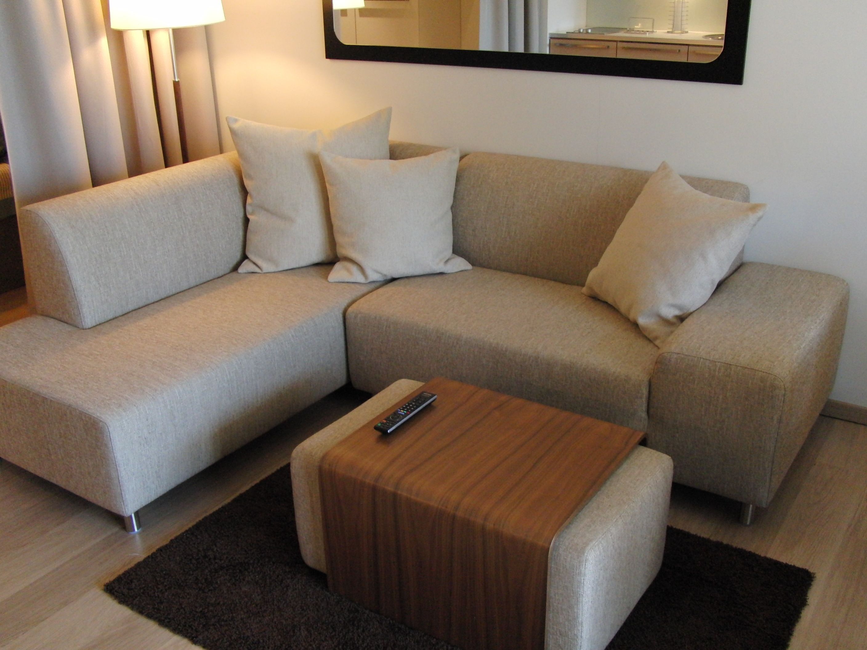 A modern living room with a beige sectional sofa, a wooden coffee table, and a dark rug.