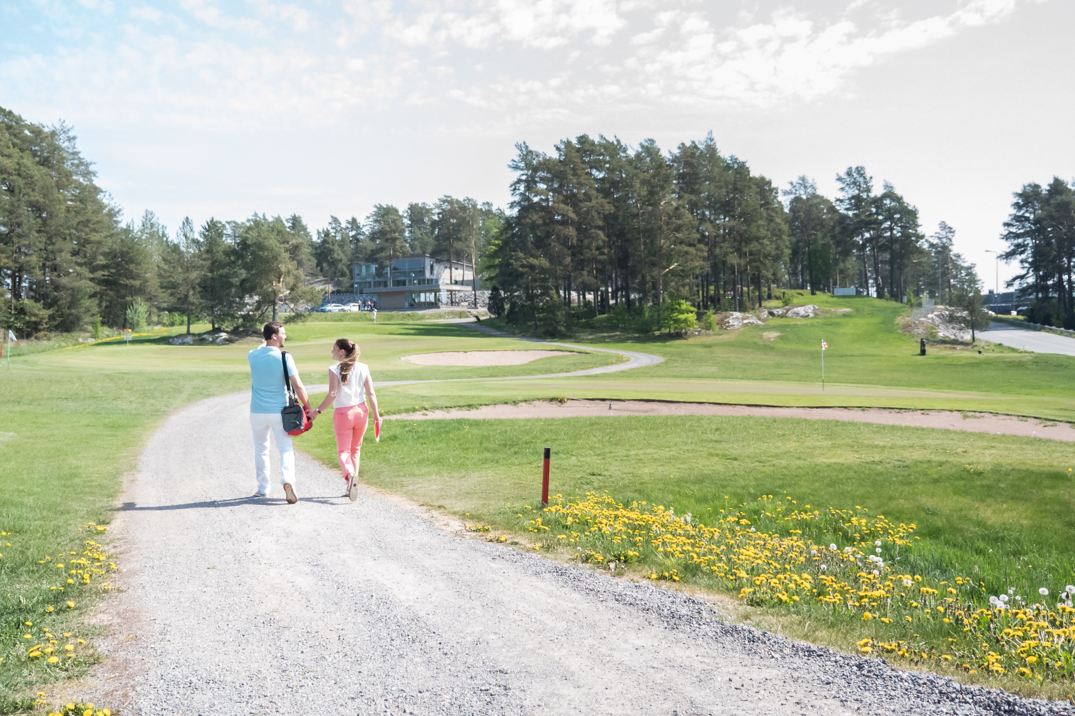 A gravel path leading to a golf course with a building in the background.