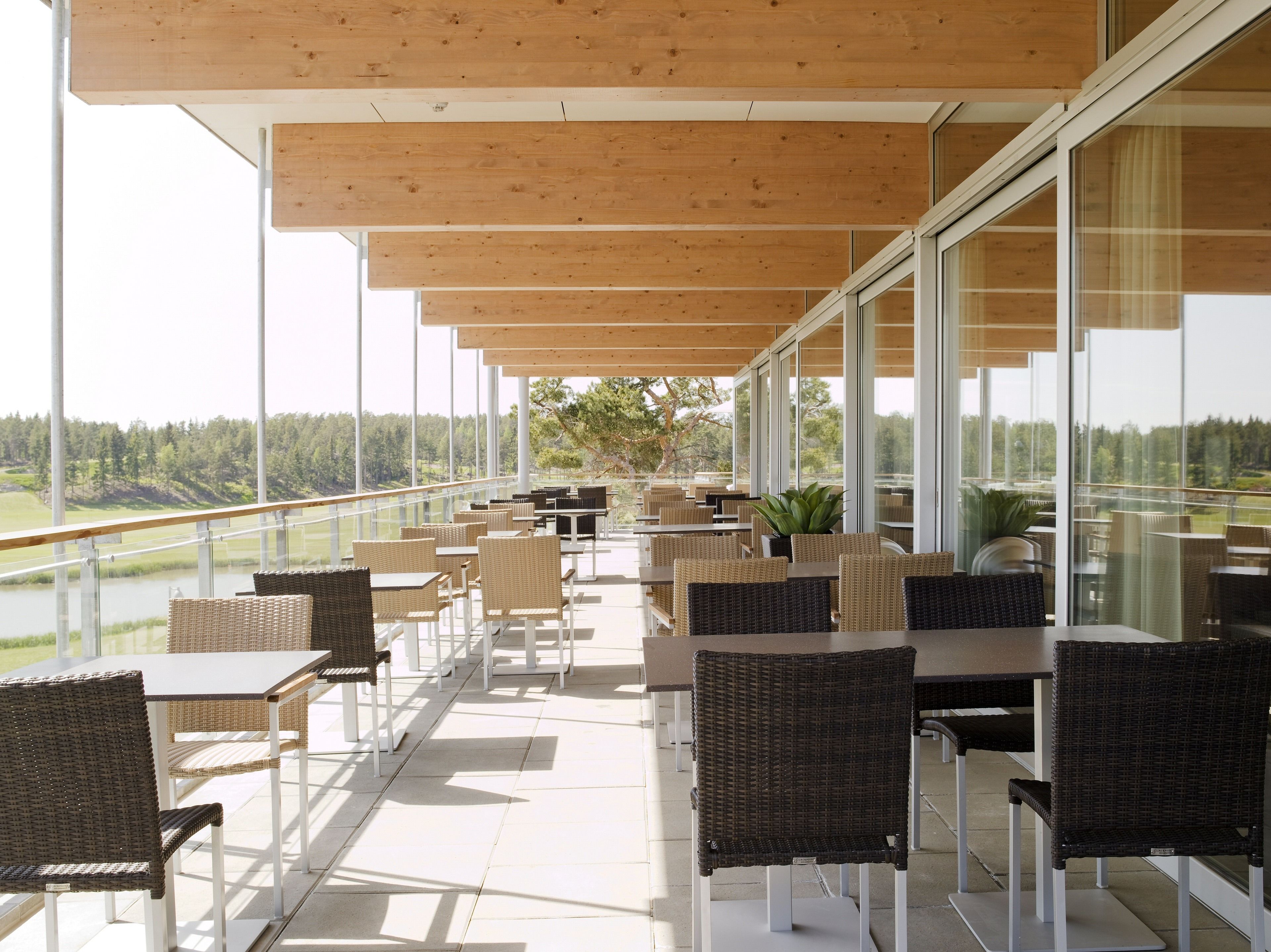 A covered outdoor seating area with wicker furniture and large windows offering a view of a forested landscape.