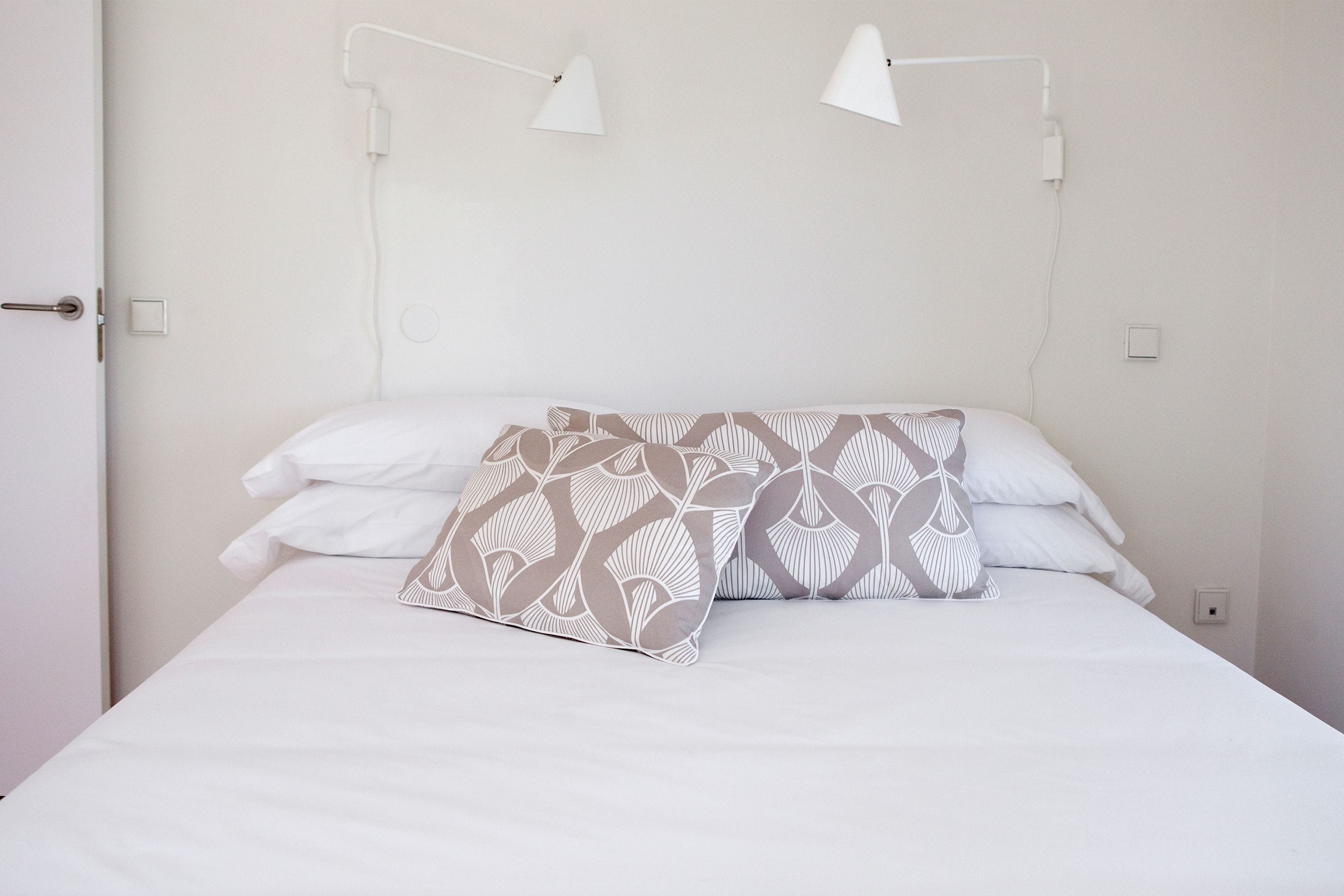 A bed with white bedding and patterned pillows, two bedside lamps, and a white door.