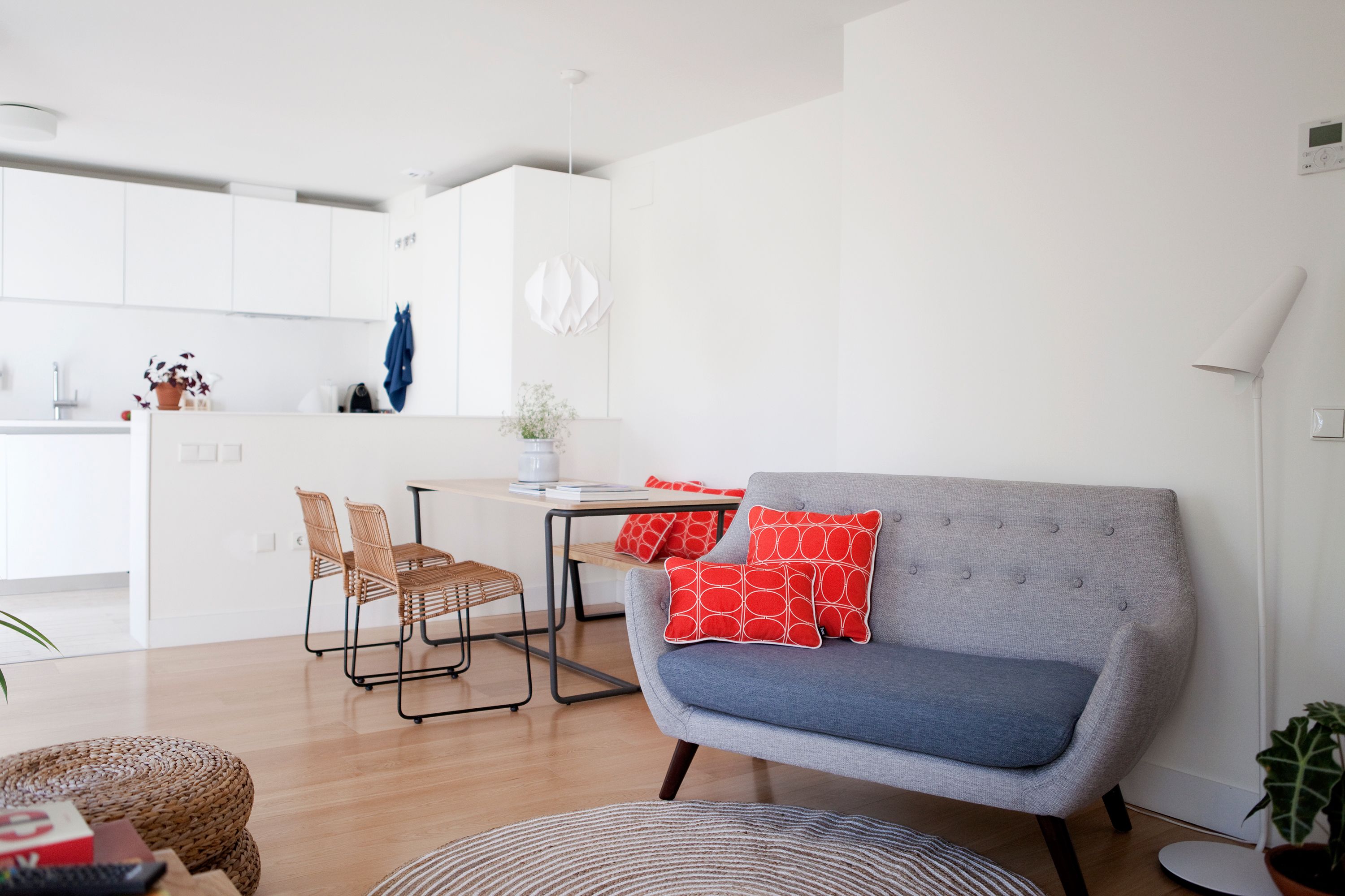 Una sala de estar moderna con un sofá gris, almohadas rojas y un comedor con una mesa y sillas.