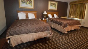 A hotel room with two beds, a wooden headboard, a lamp, and a window with curtains. - Executive Inn (Snyder)