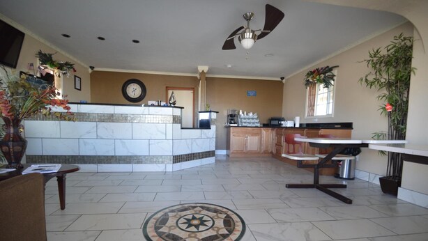 A hotel lobby with a reception desk, a clock, a coffee machine, and a dining area. - Executive Inn (Snyder)