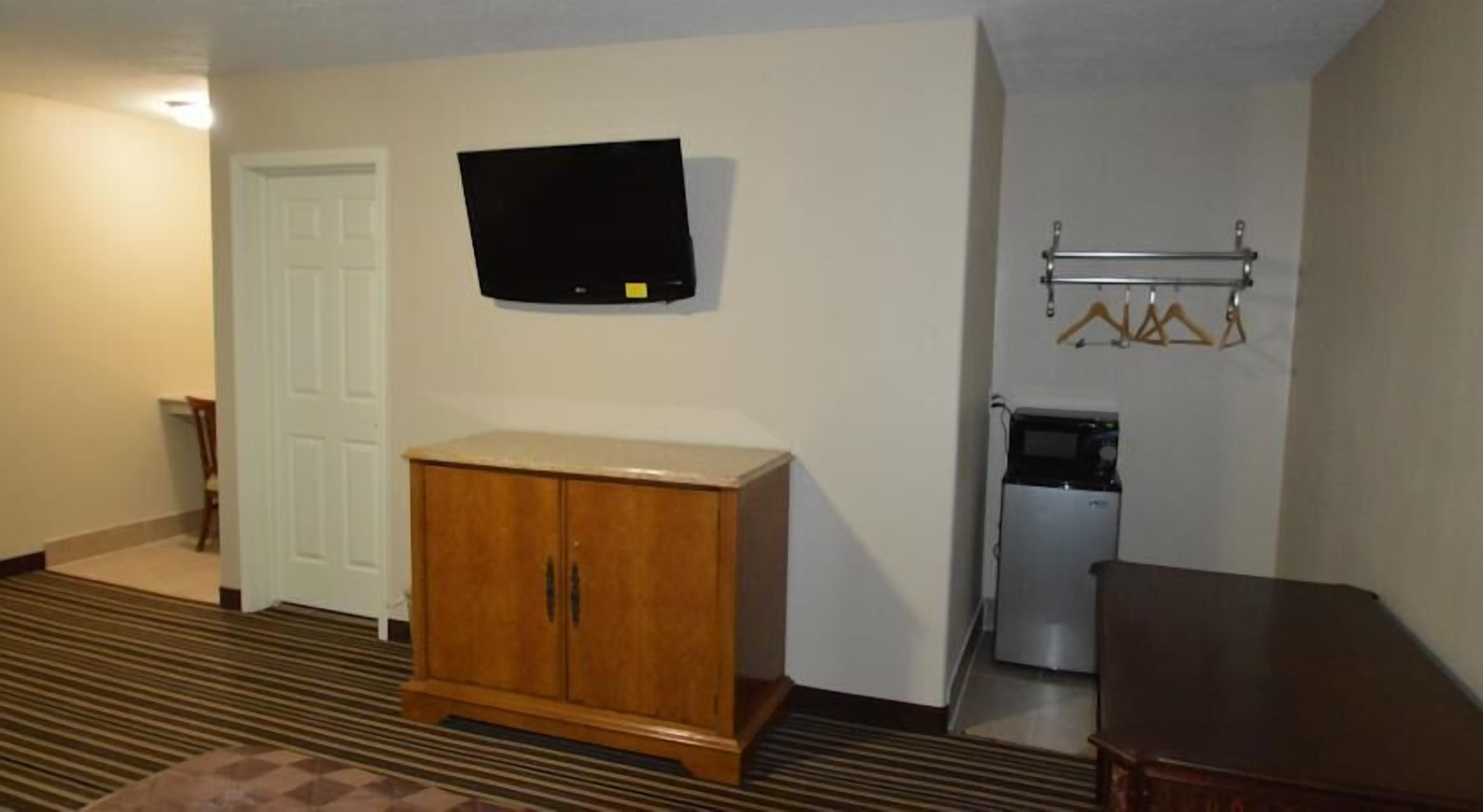 A hotel room with a wooden cabinet, a flat-screen TV mounted on the wall, a refrigerator, and a microwave.