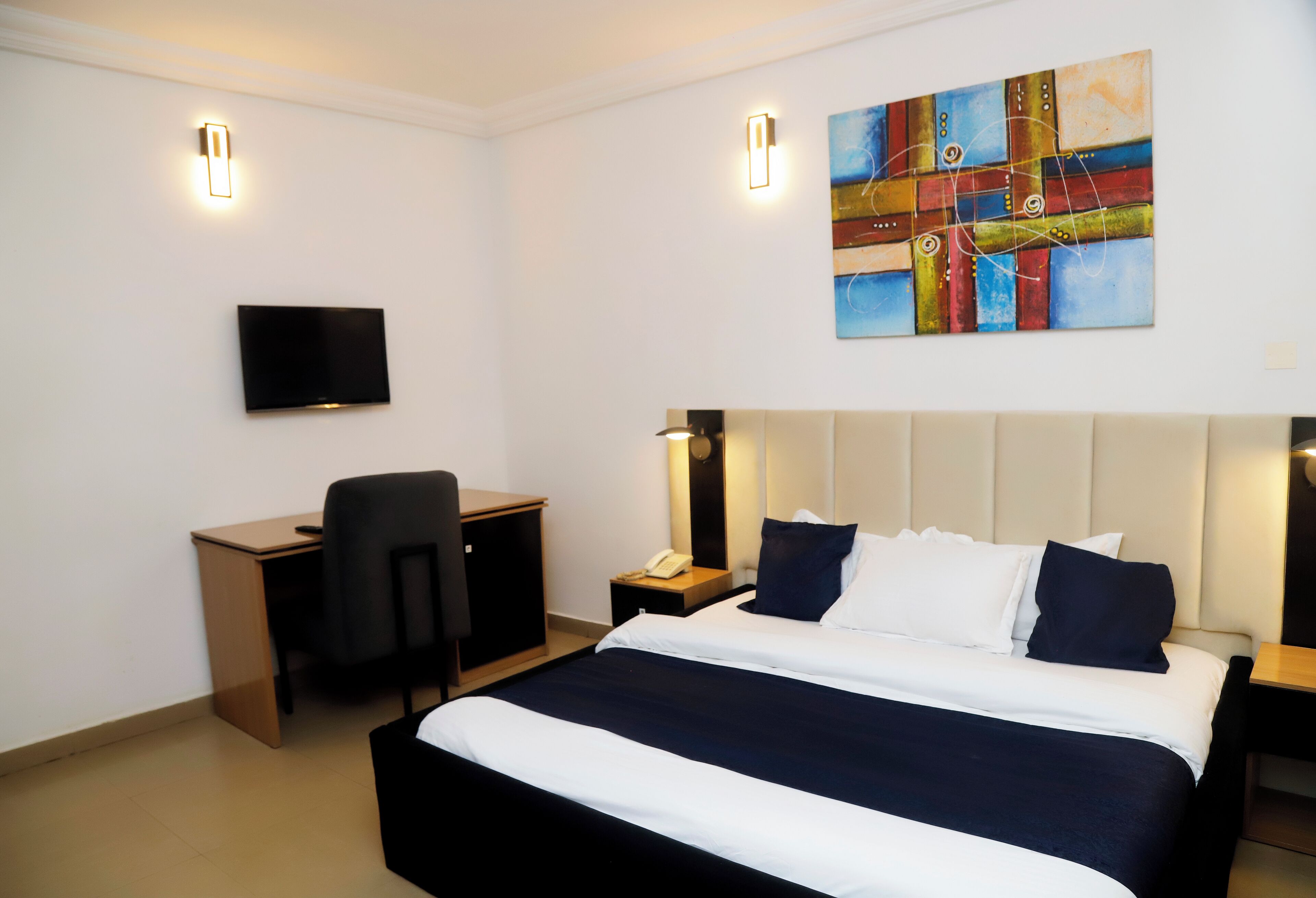 Habitación de hotel con cama, escritorio, silla, televisor y obras de arte en la pared.