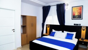 A neatly arranged bedroom with a bed, wardrobe, bedside tables, and a painting on the wall. - Western Dreams Hotel (Abuja)