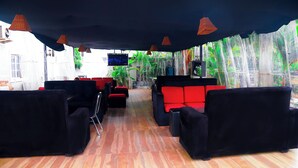 A room with black and red sofas, a television, and a view of greenery outside. - Western Dreams Hotel (Abuja)
