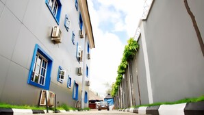 A narrow street with buildings on either side, featuring blue-framed windows and air conditioning units. - Western Dreams Hotel (Abuja)