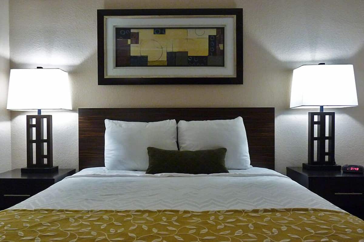 A hotel room with a neatly made bed, two bedside tables with lamps, a framed abstract artwork on the wall, and a patterned bedspread.