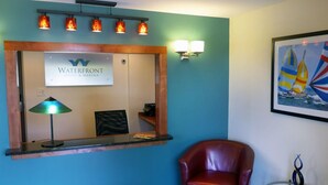 A reception area with a sign for 'Waterfront Hotel & Marina', a reception desk, a red leather chair, and a small table with a decorative item. - Waterfront Hotel and Marina (McHenry)