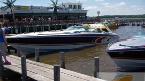 A marina with several boats docked, a wooden pier, and a building with signage in the background. - Waterfront Hotel and Marina (McHenry)
