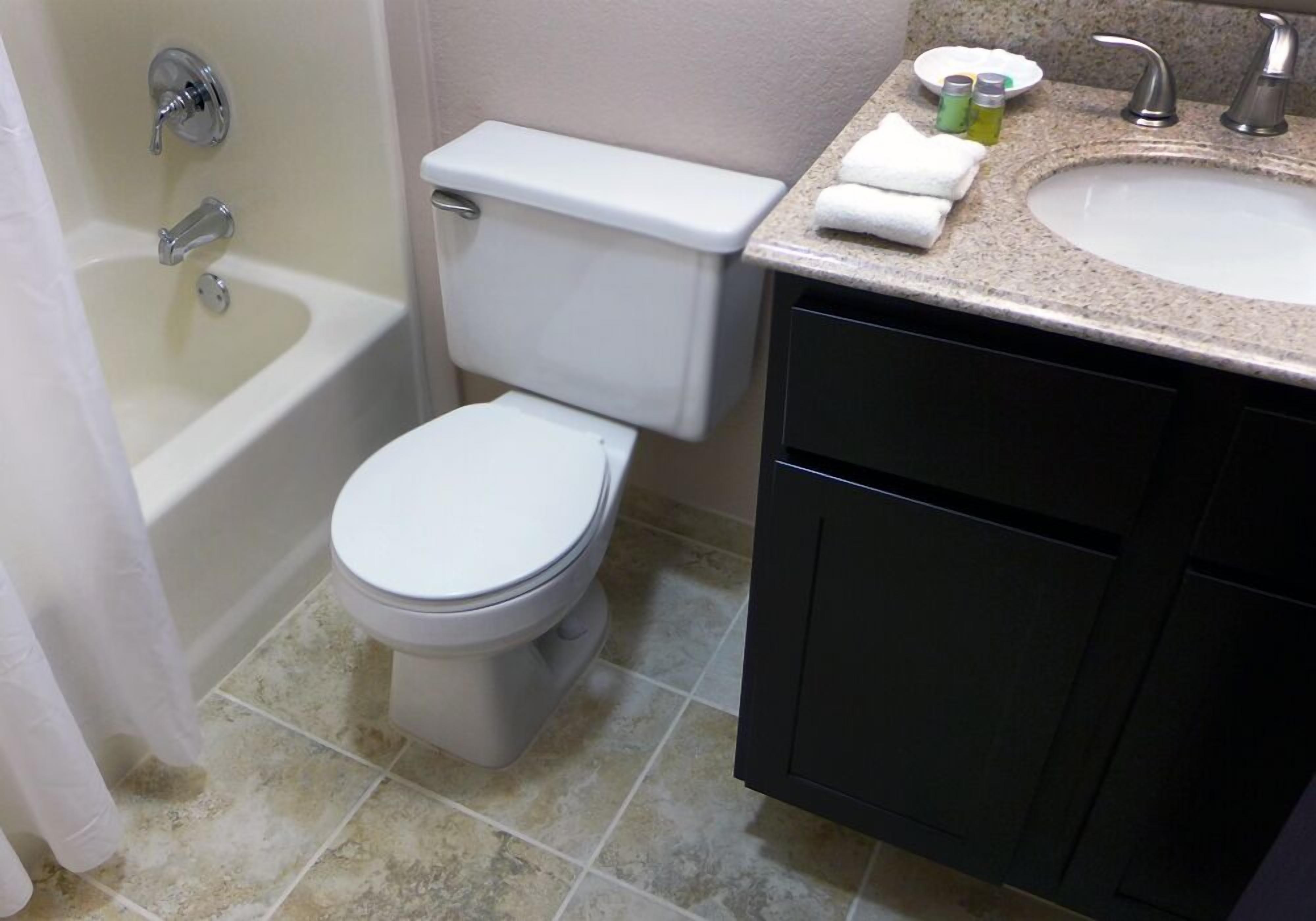 Un baño con inodoro, bañera, lavamanos y armarios oscuros.