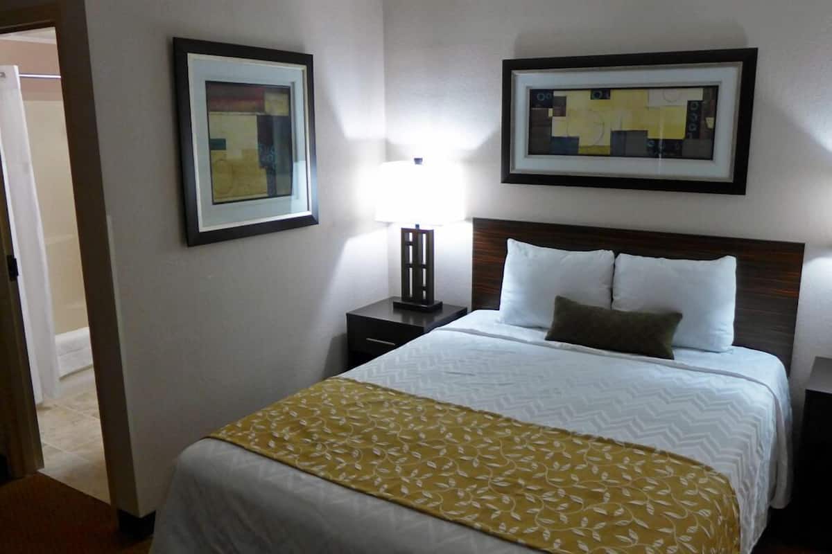 A hotel room with a large bed, a nightstand, a lamp, and two framed artworks on the wall.