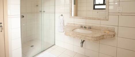 A bathroom with a glass shower enclosure, a sink with a marble countertop, and a mirror with a window above it.