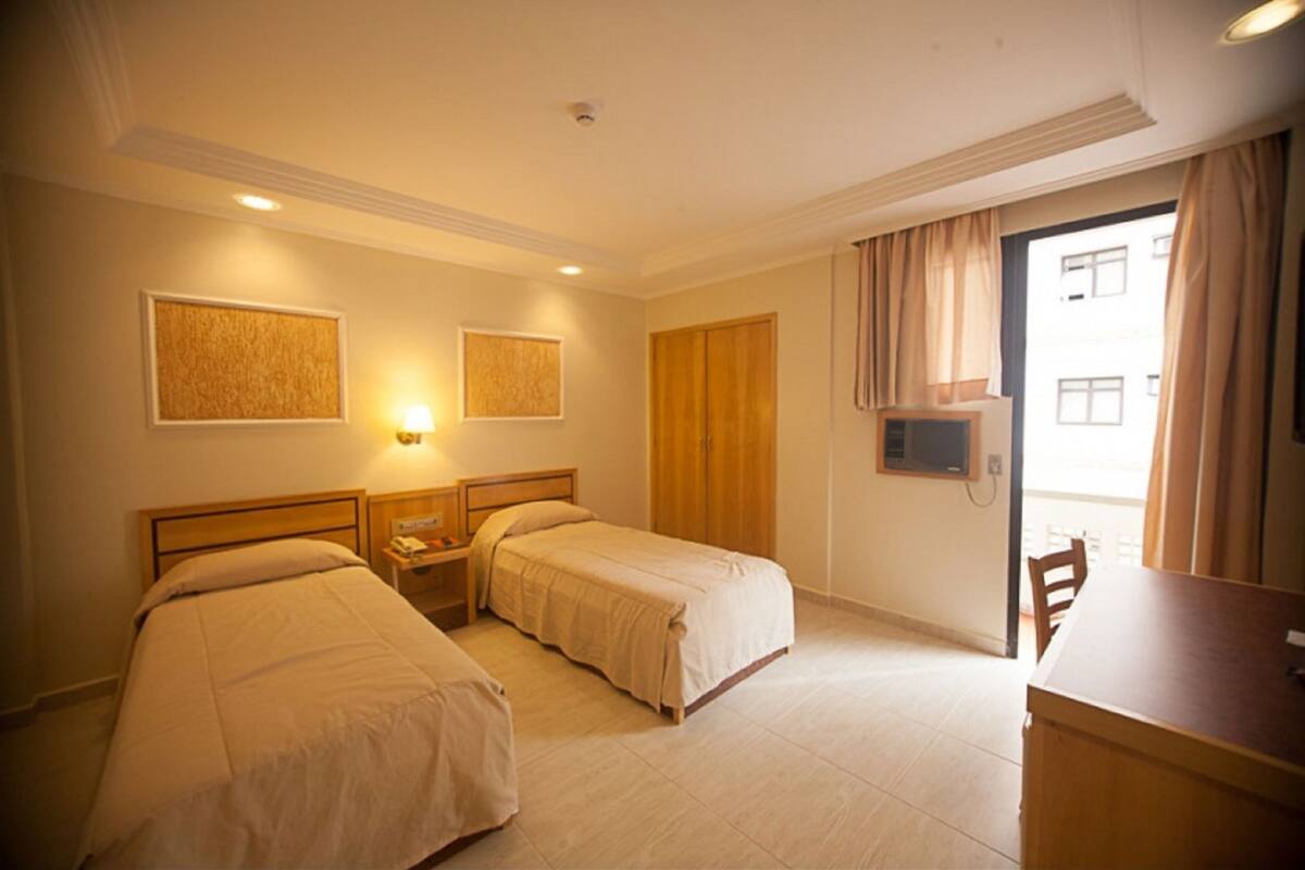 A hotel room with two beds, a desk, and a view of the outside.