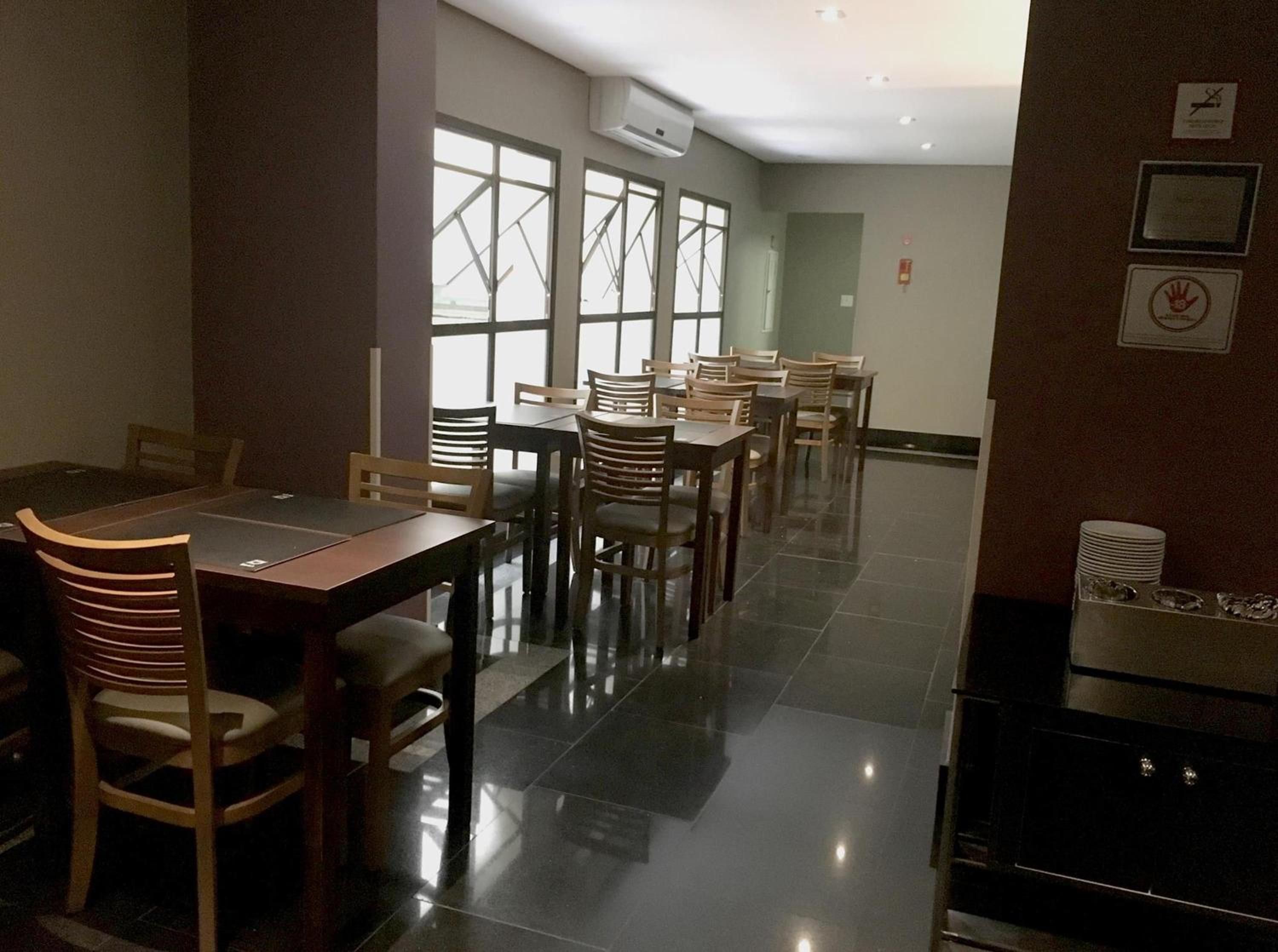 Un comedor con varias mesas y sillas, una cocina con estufa, y un ventanal con vistas al exterior.
