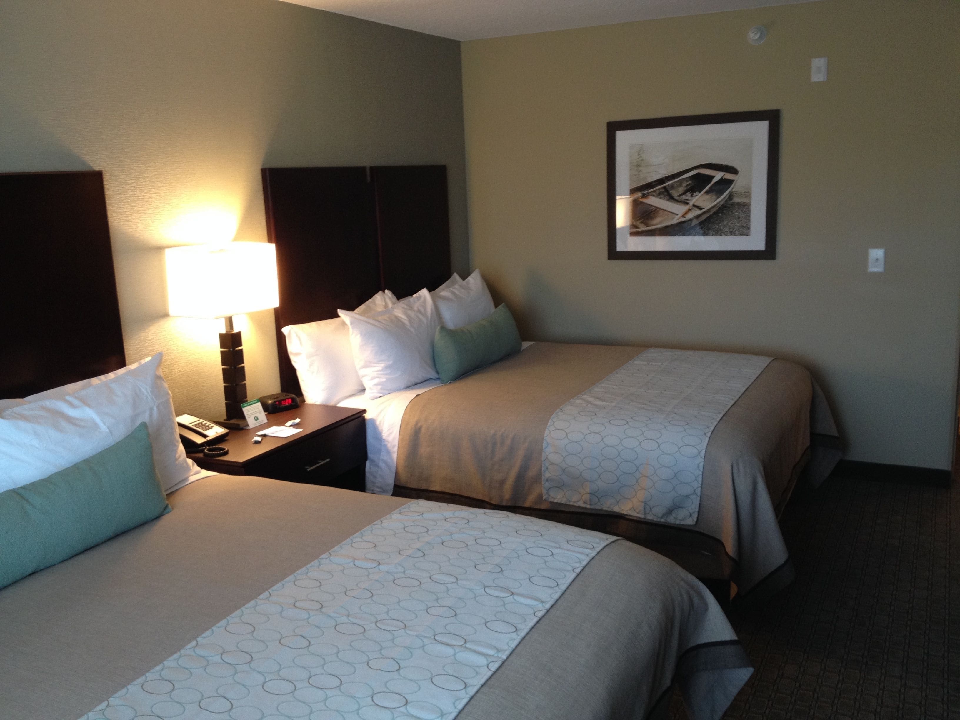 A hotel room with two beds, a nightstand, a lamp, and a framed picture on the wall.