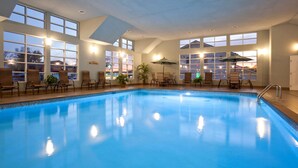 An indoor swimming pool with clear blue water, surrounded by windows and chairs. - GrandStay Hotel & Suites (Glenwood)
