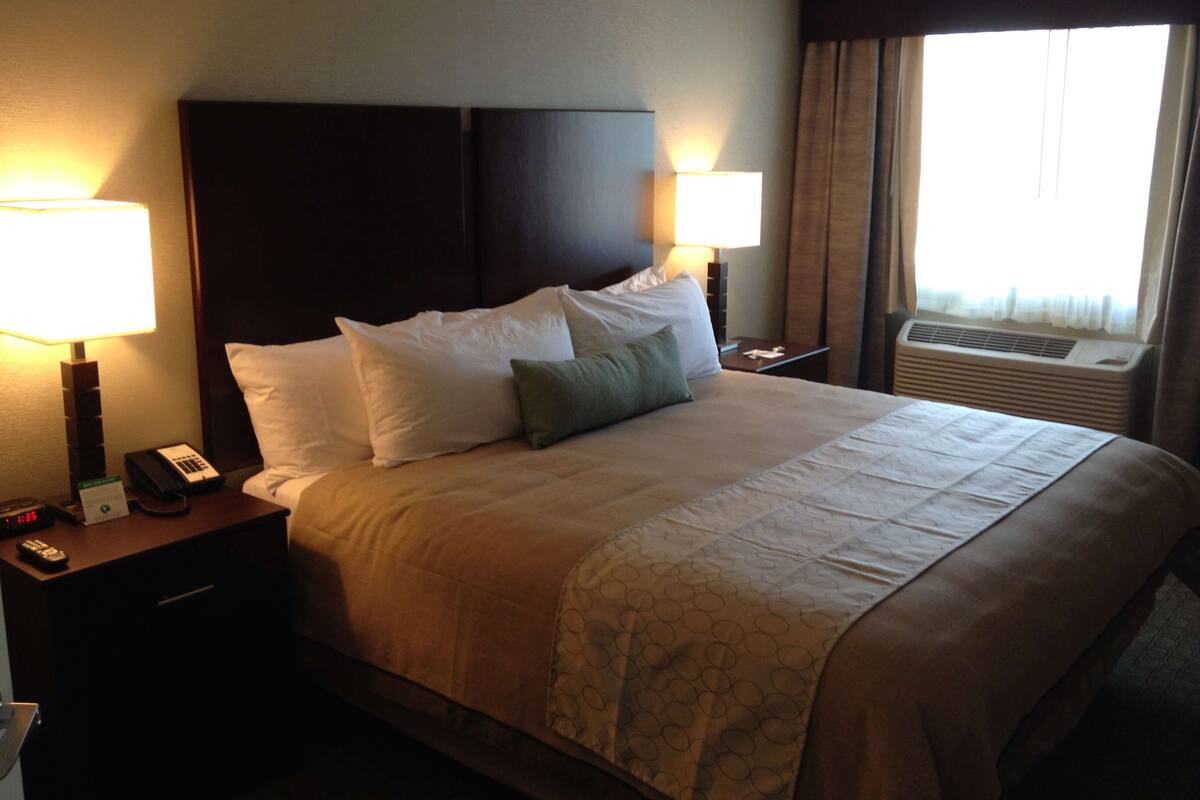 A hotel room with a large bed, two bedside tables, a nightstand, a lamp, a phone, and an air conditioning unit.