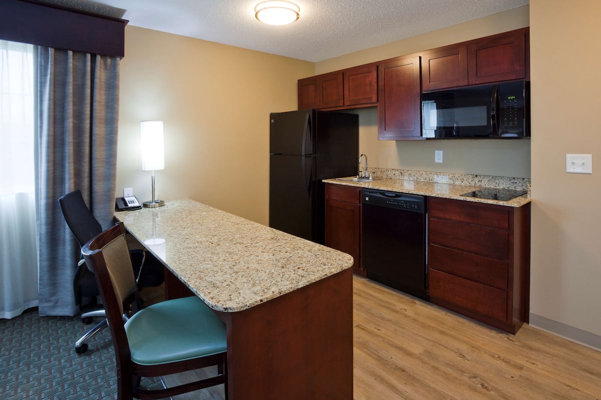 A compact kitchen with a refrigerator, microwave, and dishwasher. A small island with a chair is in the center.