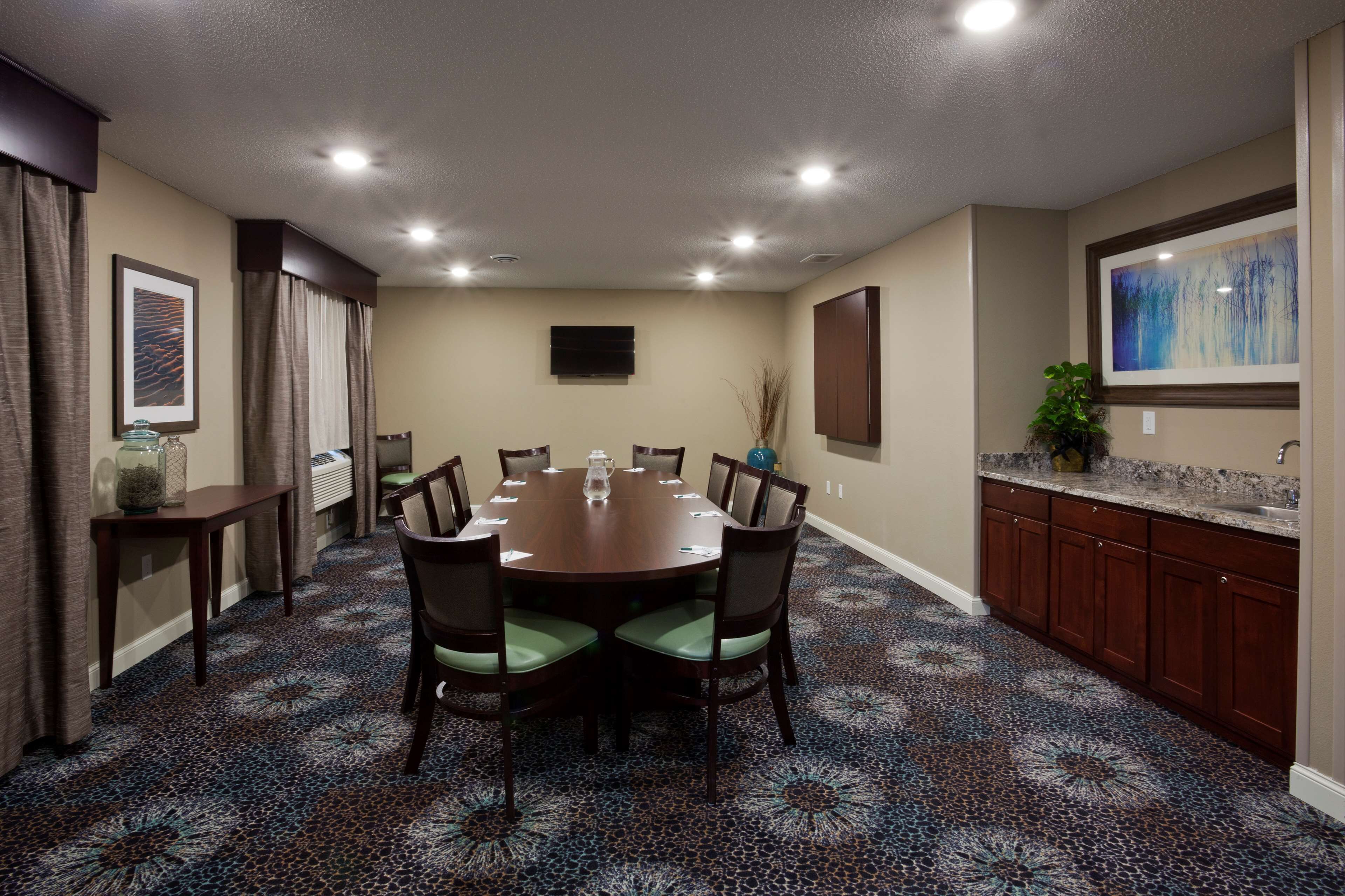A conference room with a round table, chairs, a television, and a patterned carpet.