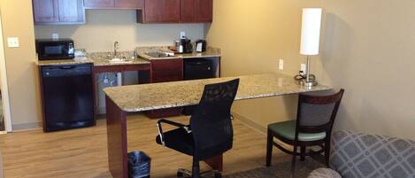 A compact kitchen with a microwave, dishwasher, and granite countertop. There is a small dining area with a chair and a table.