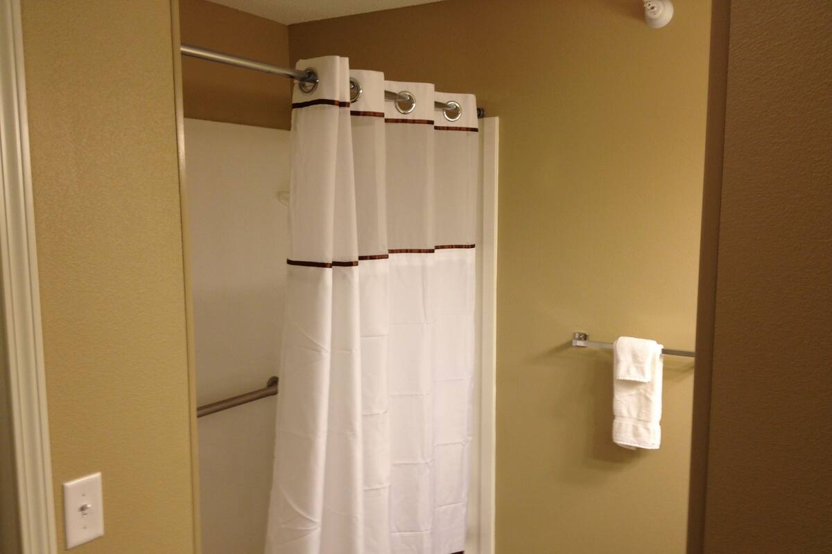 A bathroom with a white shower curtain, a towel rack with a towel, and beige walls.