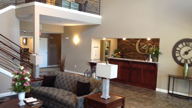 A spacious lobby with a high ceiling, a reception desk, a staircase, and a patterned sofa. - GrandStay Hotel & Suites (Glenwood)