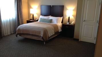 A hotel room with a large bed, two bedside tables with lamps, a door, and a window with curtains.