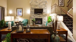 A living room with a stone fireplace, a flat-screen TV, a staircase, and a sofa. - GrandStay Hotel & Suites (Glenwood)