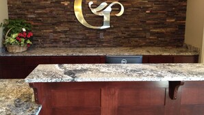 A reception desk with a stone wall backdrop, a large illuminated 'G' sign, and a potted plant with red flowers. - GrandStay Hotel & Suites (Glenwood)
