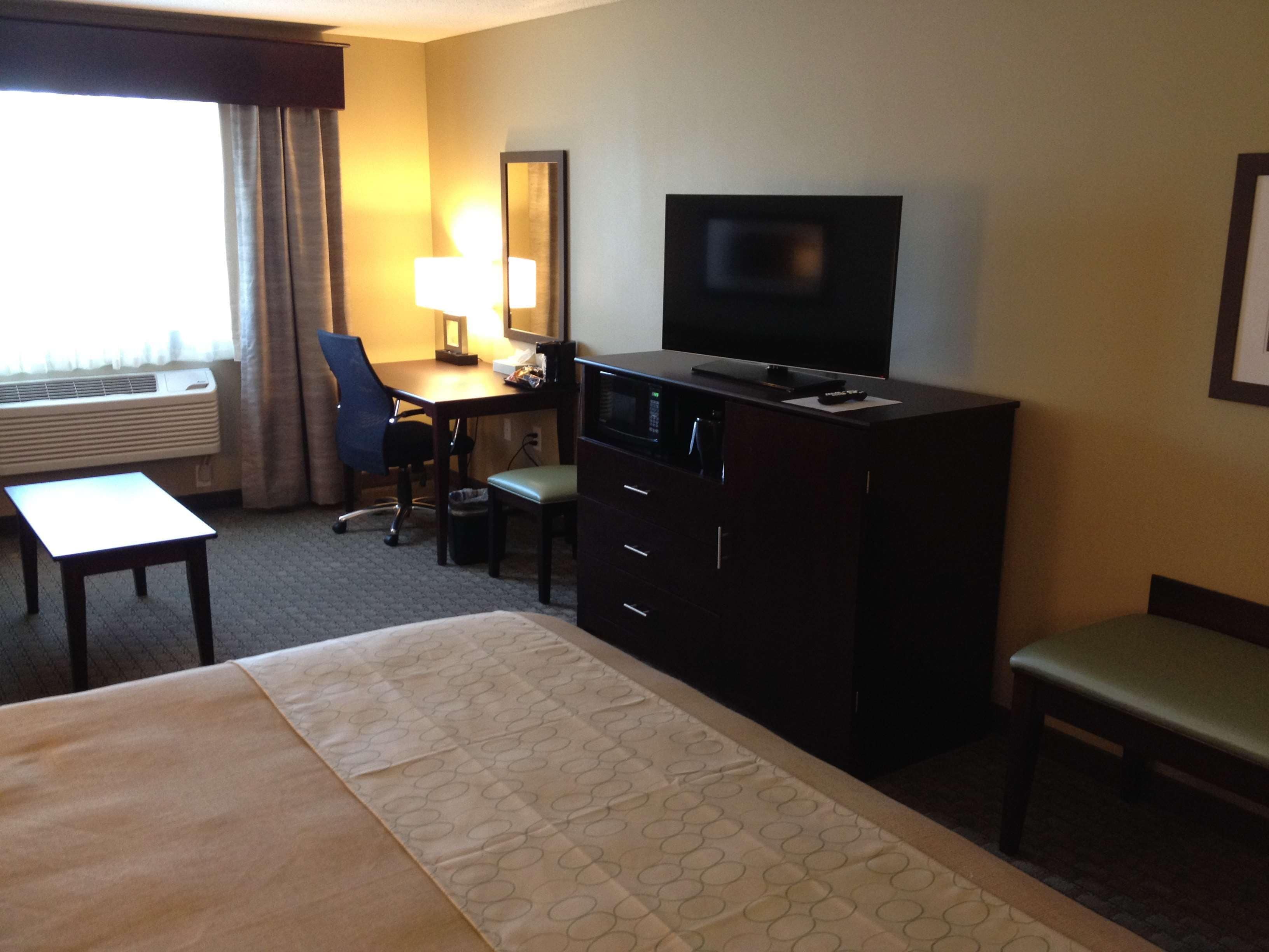 A hotel room with a bed, a desk with a chair, a television, and a window with curtains.