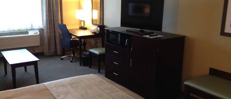 A hotel room with a bed, a desk with a chair, a television, and a window with curtains.