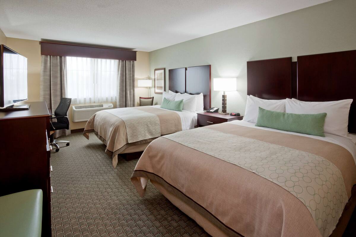 A hotel room with two beds, a desk, a chair, a TV, and a window with curtains.