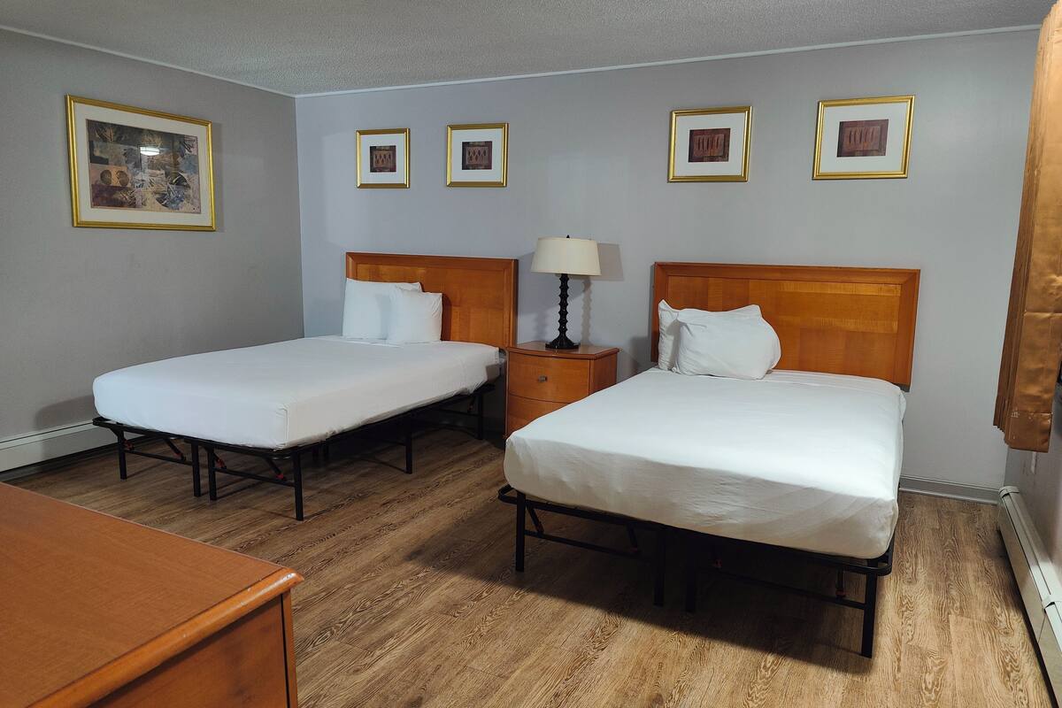 Une chambre d’hôtel avec deux lits simples, une table de chevet en bois avec une lampe et trois tableaux encadrés accrochés au mur.