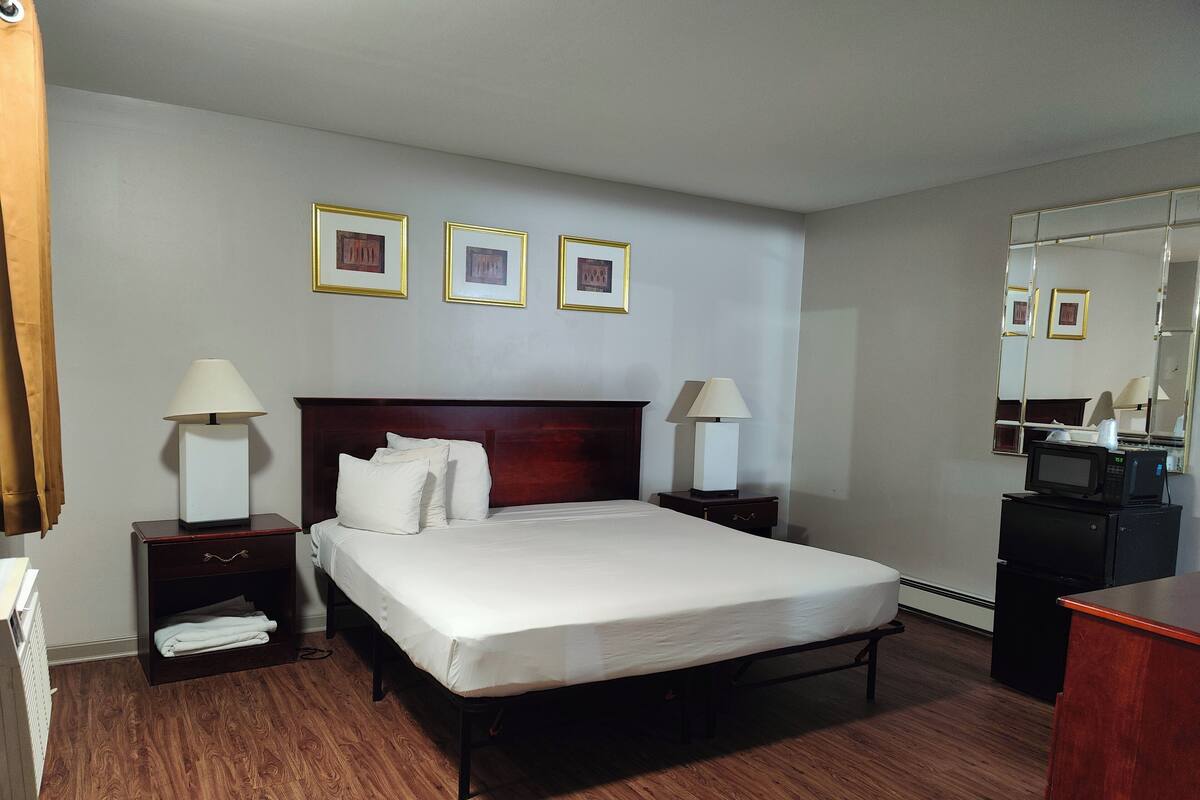 Une chambre d’hôtel avec un grand lit, deux tables de chevet avec des lampes, une commode, un miroir et trois tableaux encadrés accrochés au mur.