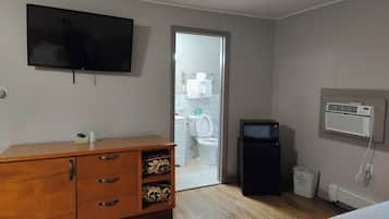 Ein Hotelzimmer mit einem Holzkasten, einem flachbildfernseher an der Wand, einer Mikrowelle und einem kleinen Heizgerät auf dem Boden.