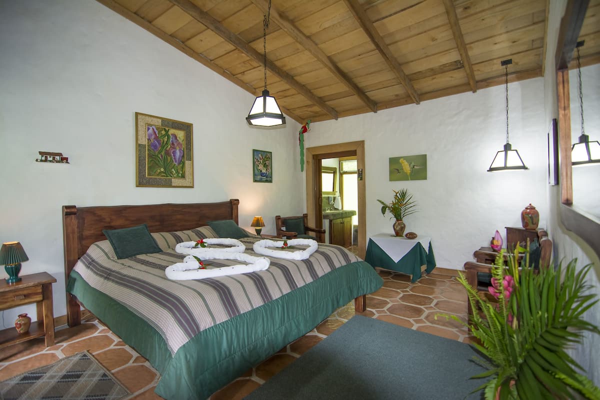 A well-lit bedroom with a large bed, a wooden ceiling, and a view of the outside.