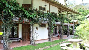 A building with a stone facade, a covered patio area, and a garden with a stone table and benches.