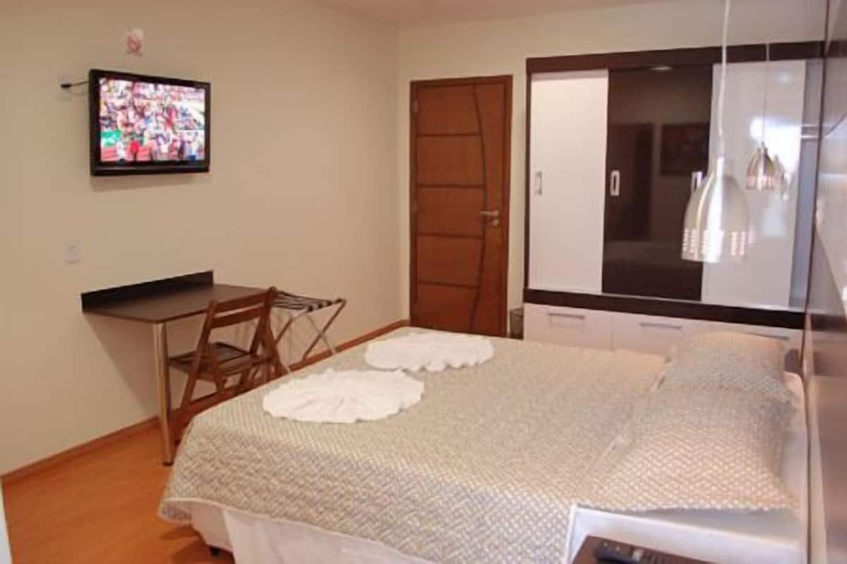 Une chambre à coucher avec un lit, un bureau, une chaise, une armoire et un téléviseur fixé au mur.
