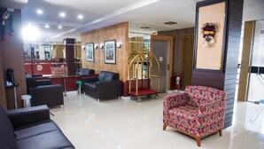 Een hotel lobby met een receptiebalie, een zithoek met banken en een kleurrijke fauteuil, en een decoratief wandobject.