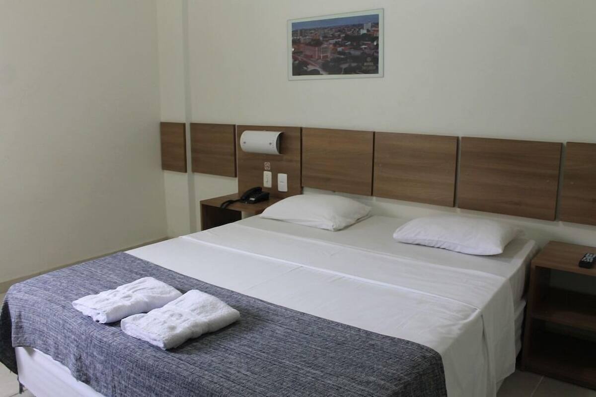 Une chambre d’hôtel avec un lit, une table de chevet, une télécommande et un tableau au mur.