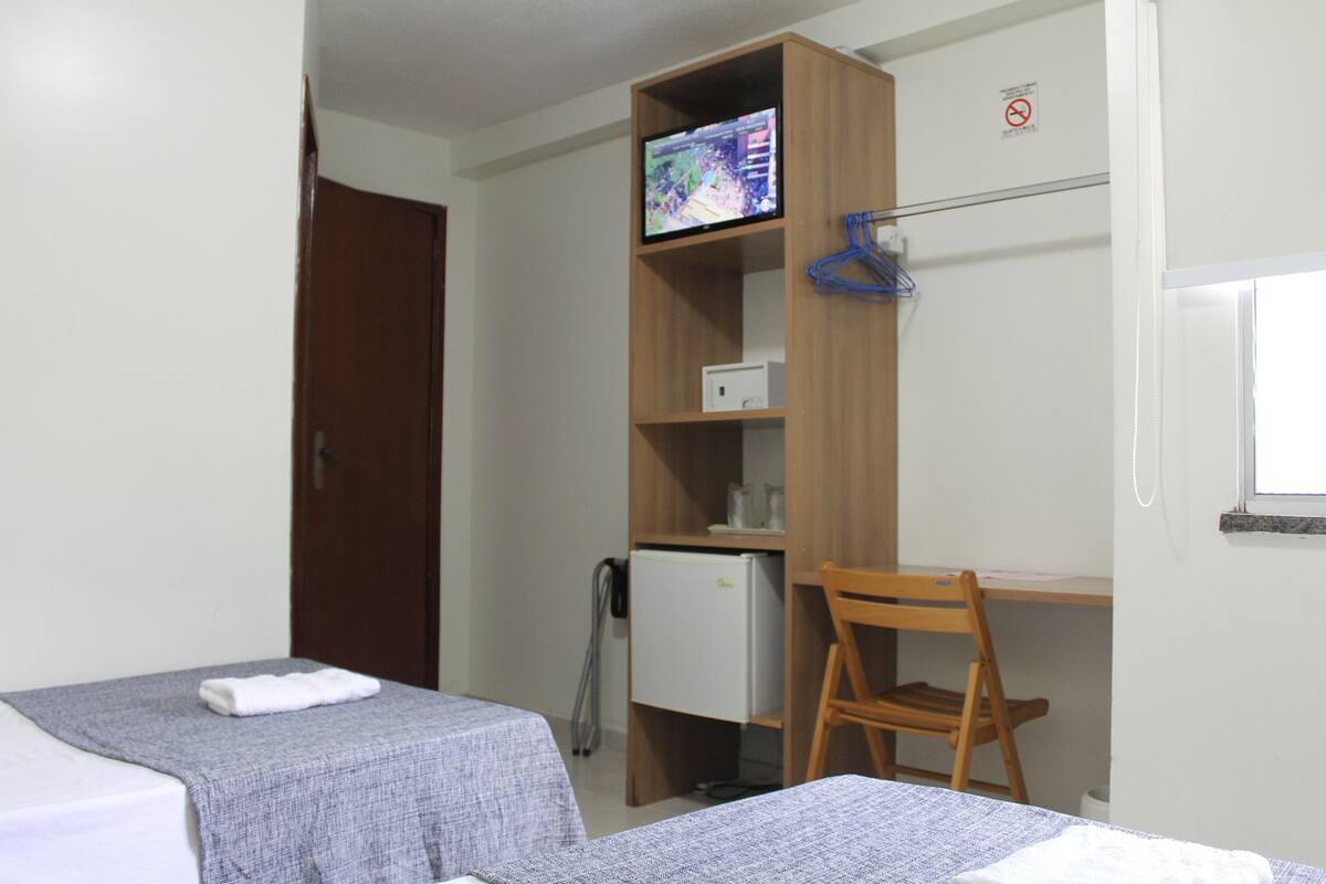 Une chambre d’hôtel avec deux lits, un bureau, une télévision, un réfrigérateur et une chaise.