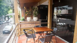 Een terras met een houten tafel en stoelen, plantenpotten en uitzicht op de straat.