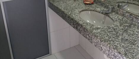 A bathroom with a granite countertop, two sinks, a toilet, and two hair dryers mounted on the wall.