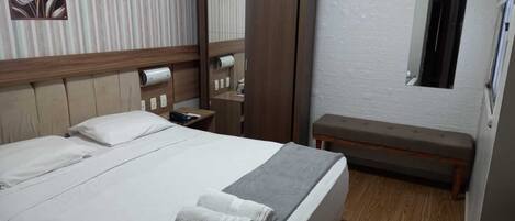 Ein Hotelzimmer mit Bett, Sitzbank, Kleiderschrank und Spiegel.