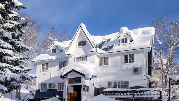 A large, two-story house covered in snow, with a visible entrance and a staircase leading to the main door. - Pension Cotton Farm (Niseko)